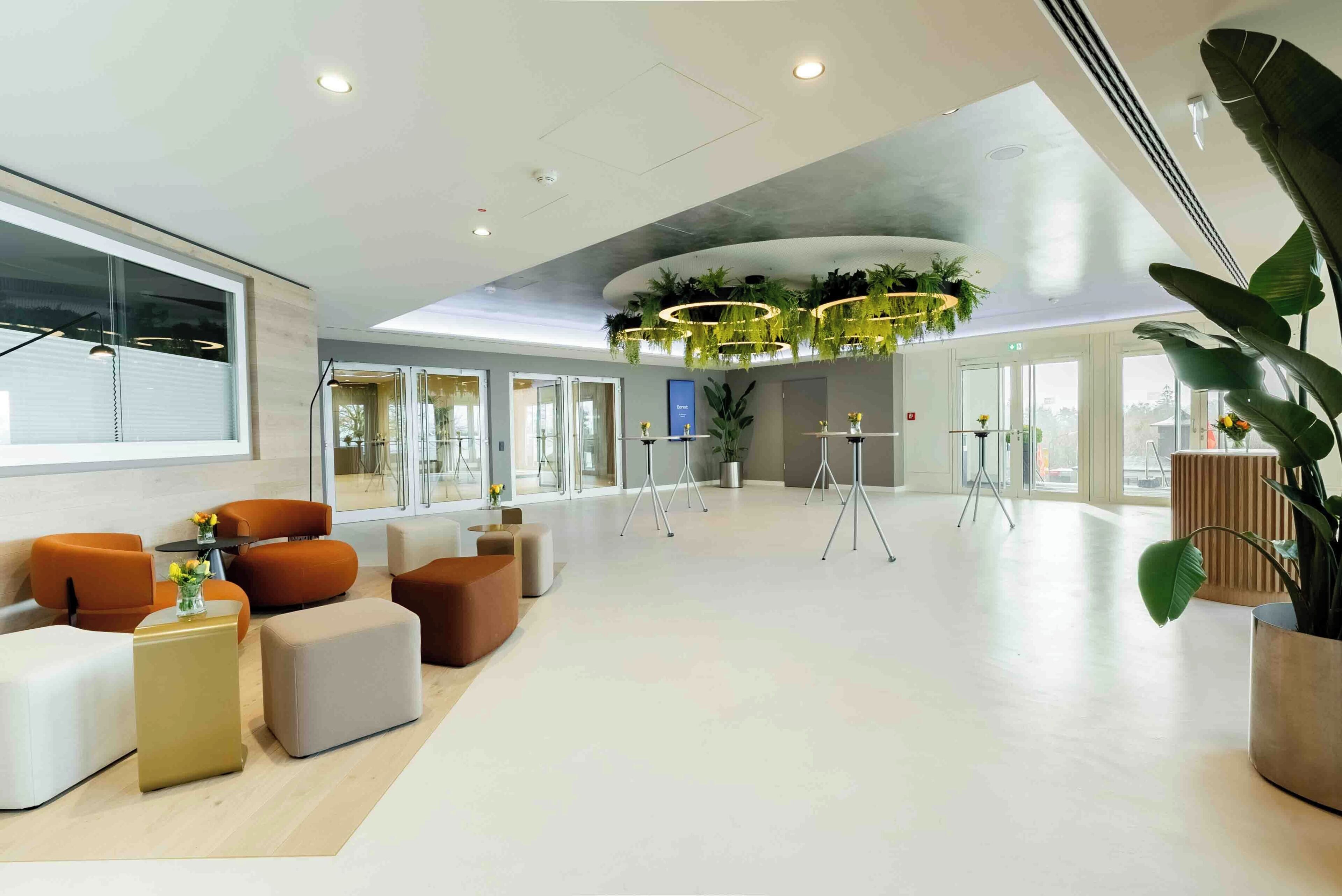 A spacious lobby with modern seating, a large window, and a ceiling with circular light fixtures.