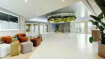 Een ruime lobby met modern meubilair, een groot raam en een plafond met ronde lampen.