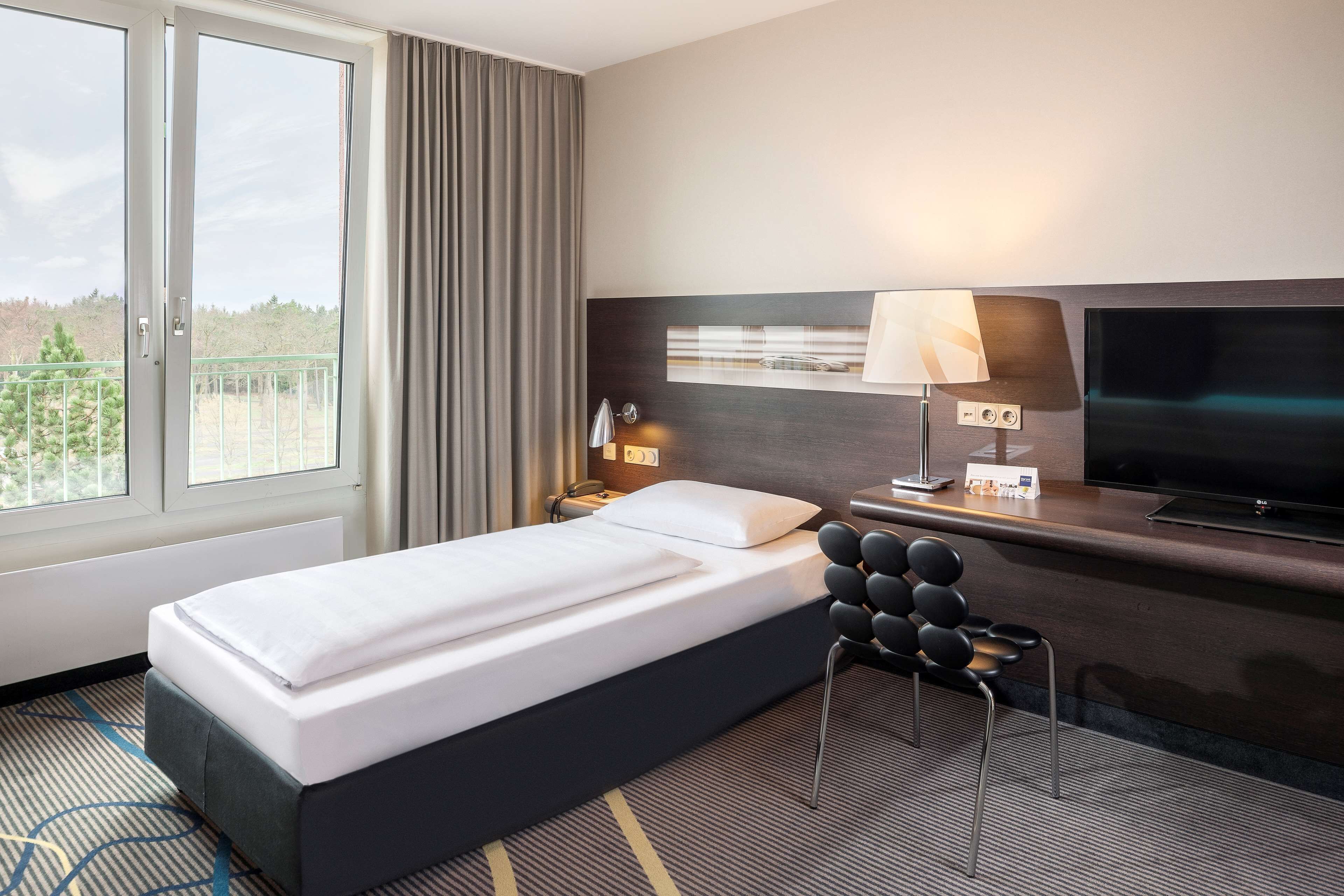 Une chambre d’hôtel avec un lit, un bureau avec une télévision, une lampe et une vue sur l’extérieur.