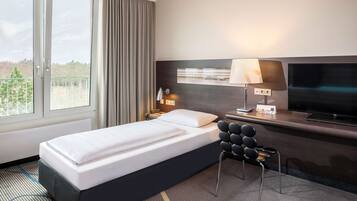 Habitación de hotel con cama, escritorio con televisor, lámpara y vista al exterior.