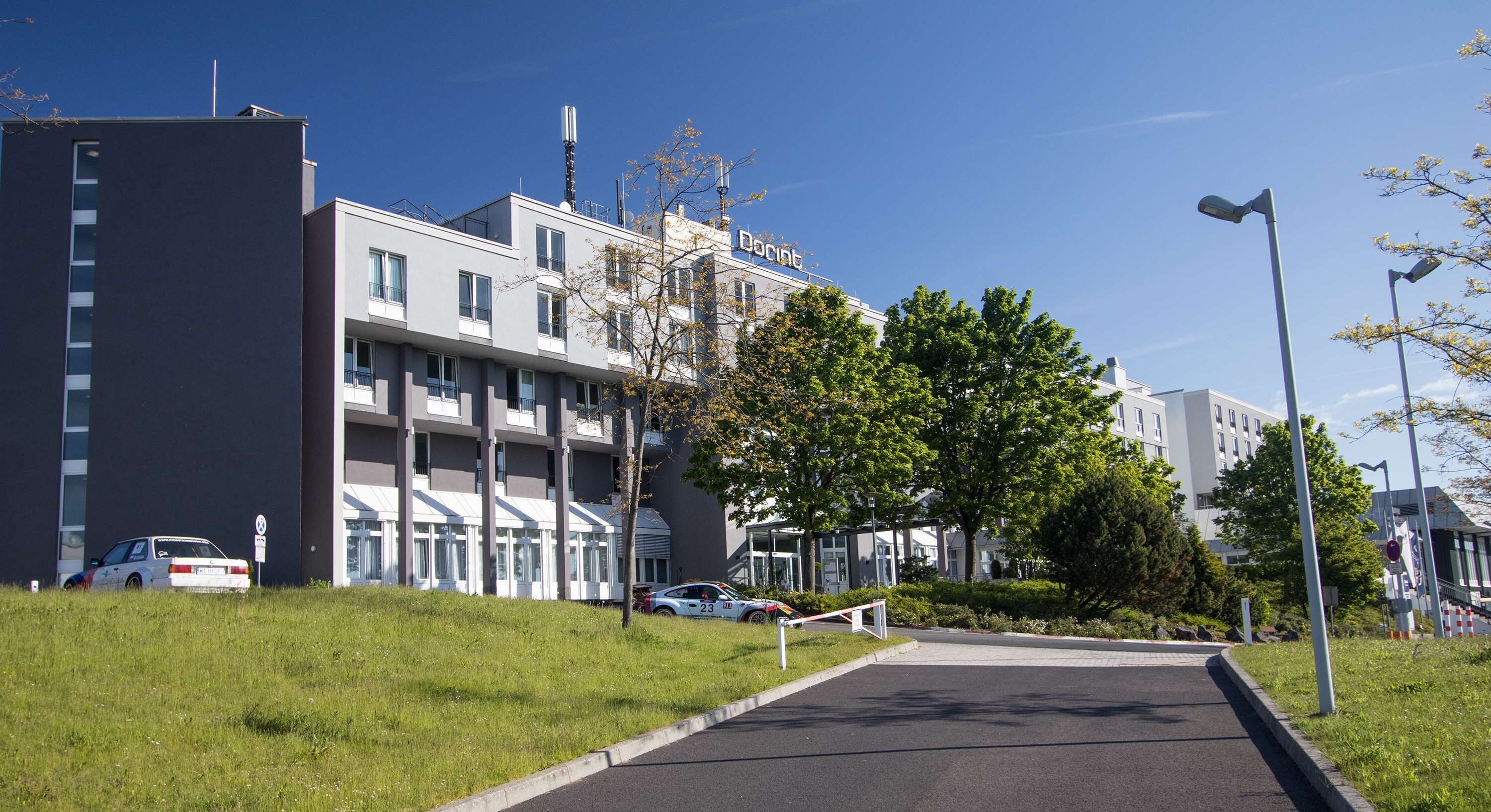 Un bâtiment moderne à plusieurs étages, doté d’un espace de stationnement et d’un chemin menant à l’entrée.