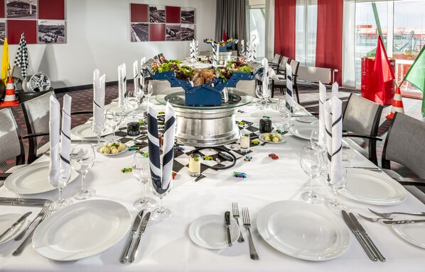 A dining table set for a formal meal with a central decorative piece, surrounded by chairs and a view of the cityscape through large windows.