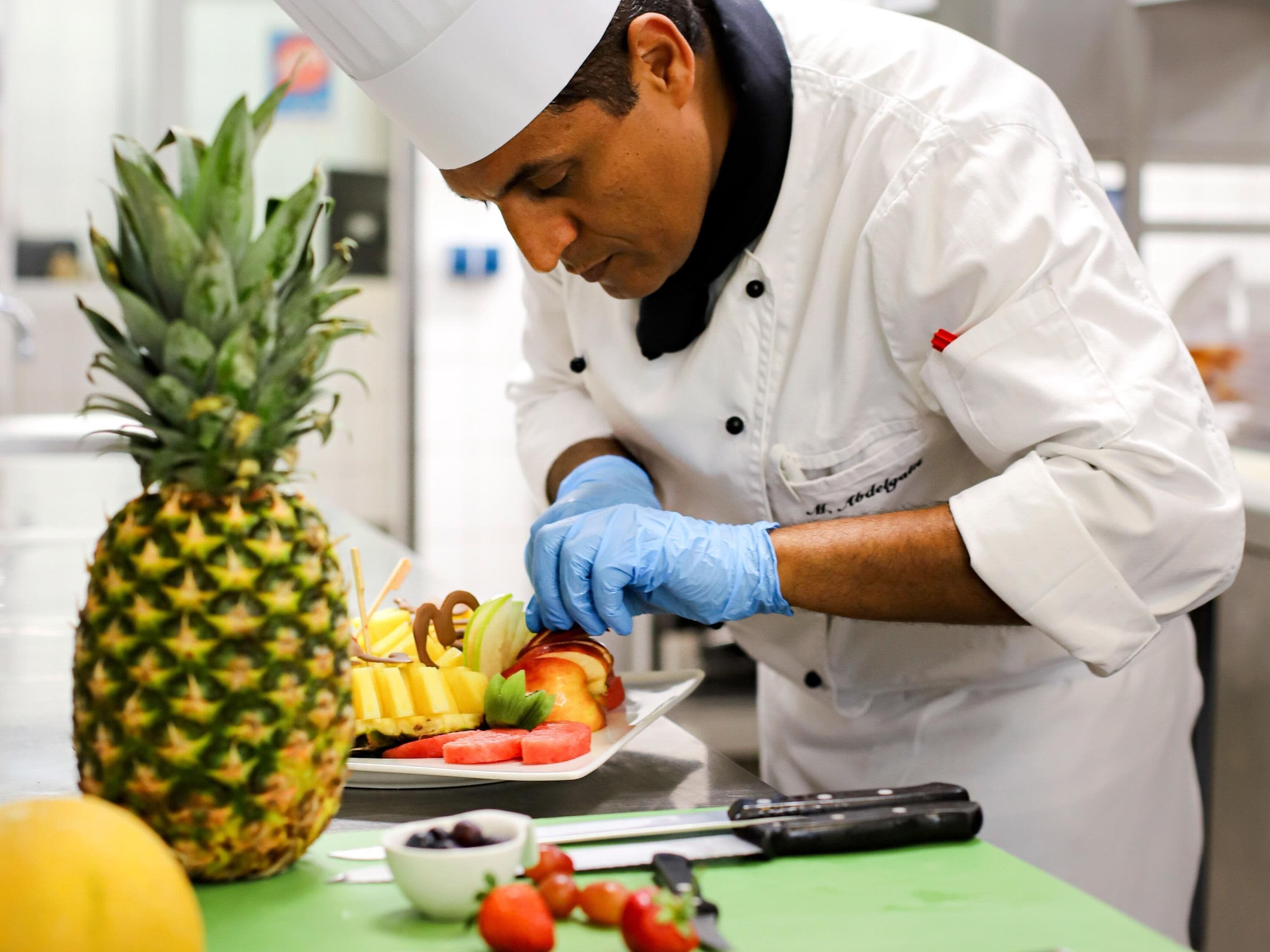 Un chef preparando una bandeja de frutas con piña, sandía y otras frutas.