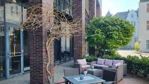 An outdoor seating area with wicker furniture and a glass door entrance. - Novotel Hannover (Hannover)