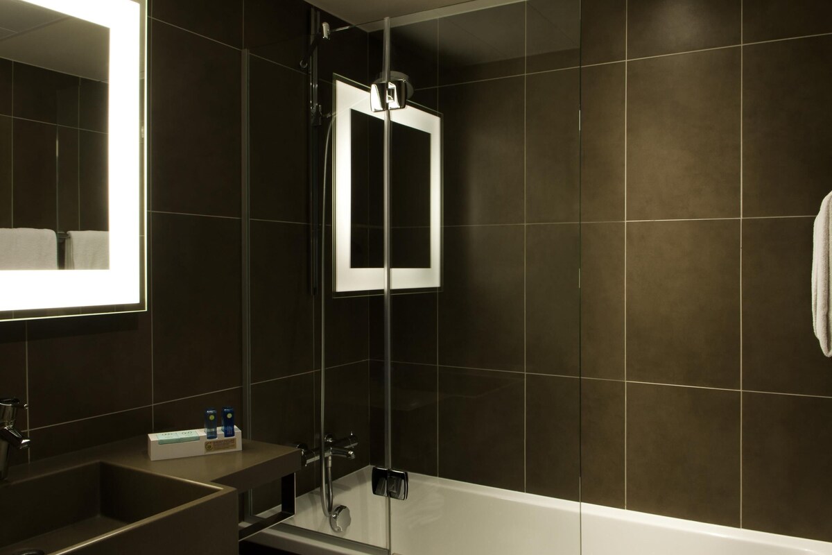 A modern bathroom with a glass-enclosed shower, a large mirror, and a white bathtub.