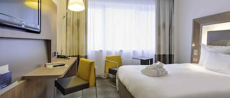 A hotel room with a bed, a desk, a chair, a TV, and a window with curtains.