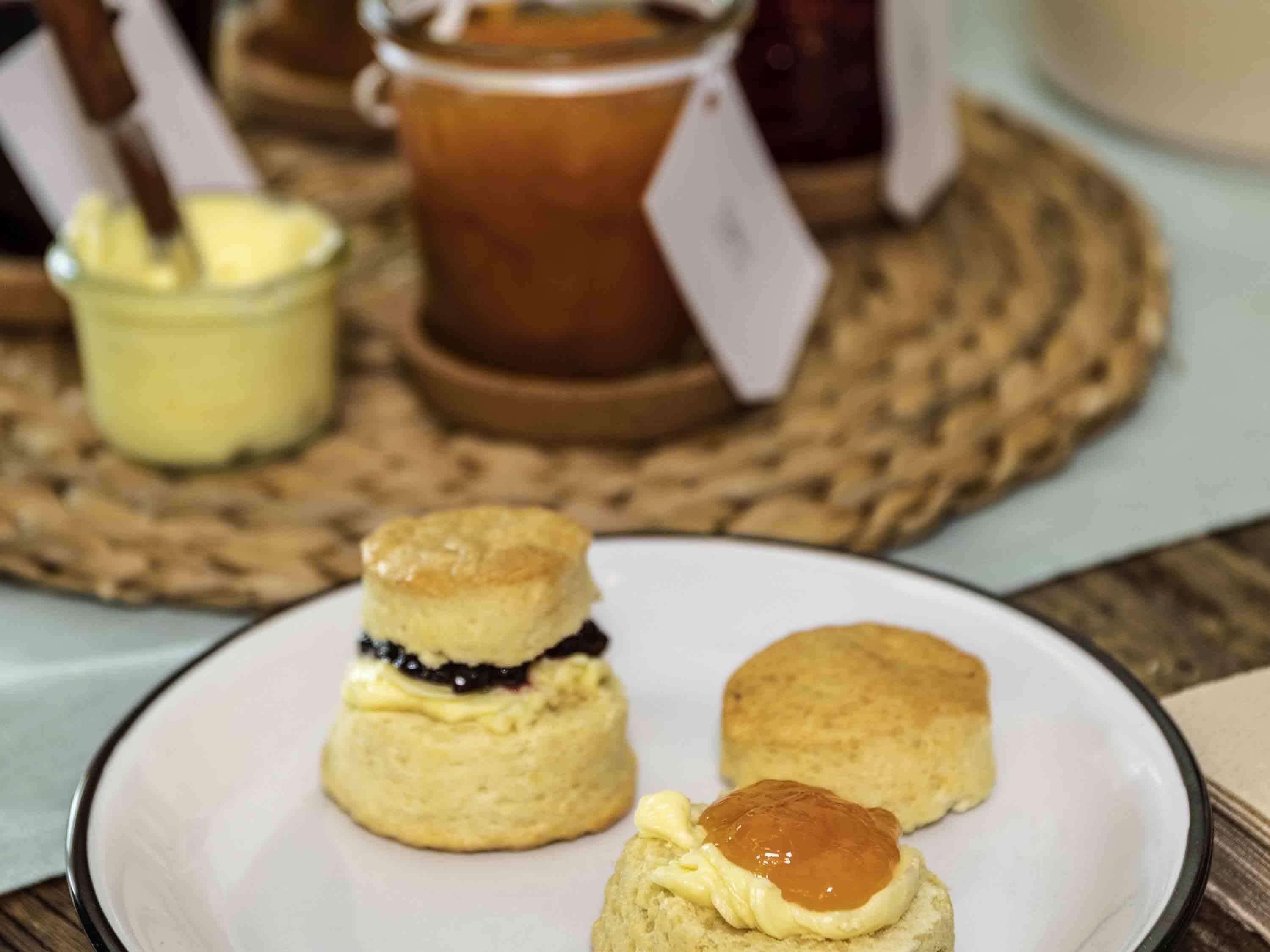 A plate with three scones, one with jam and butter, and two plain scones, on a table with a woven placemat.