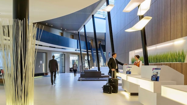 A modern hotel lobby with a reception desk, a staircase, and a large pillar. - Novotel Hannover (Hannover)