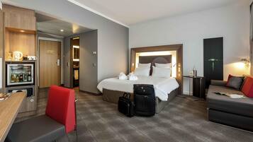 Een hotelkamer met een bed, een bureau, een stoel, een sofa, een minibar en uitzicht op zee.