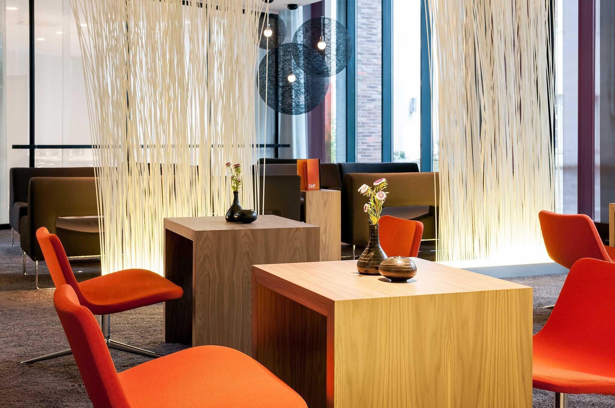Ein moderner Arbeitsraum mit orangefarbenen Stühlen, einem Holztisch und dekorativen Vasen.