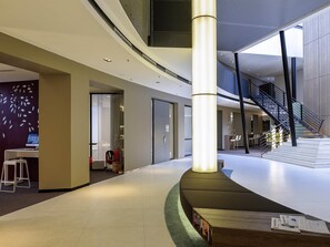 A spacious lobby with a central column, a staircase, and a reception desk.