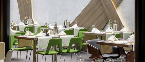 A restaurant with tables set for dining, green chairs, and a modern interior design.