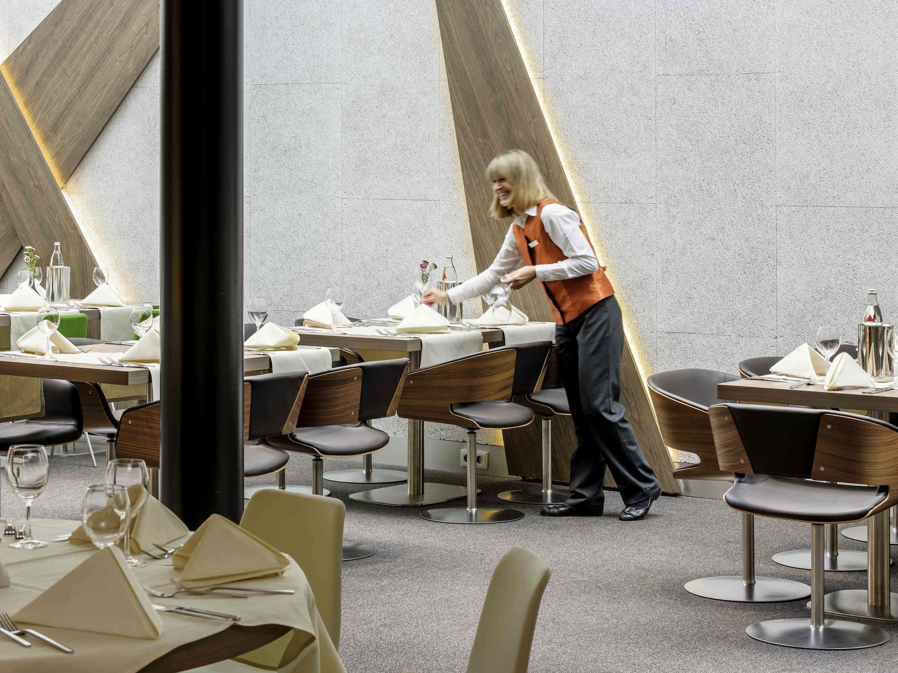 A modern dining area with tables set for service, a waiter attending to guests, and contemporary chairs.