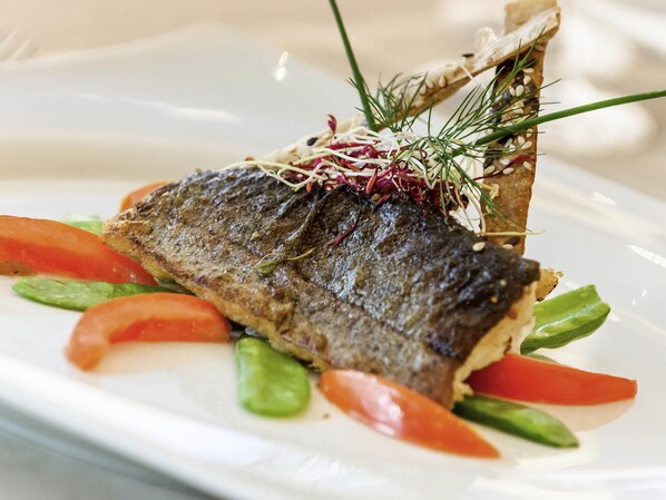 A plate with a fish, vegetables, and a decorative herb.