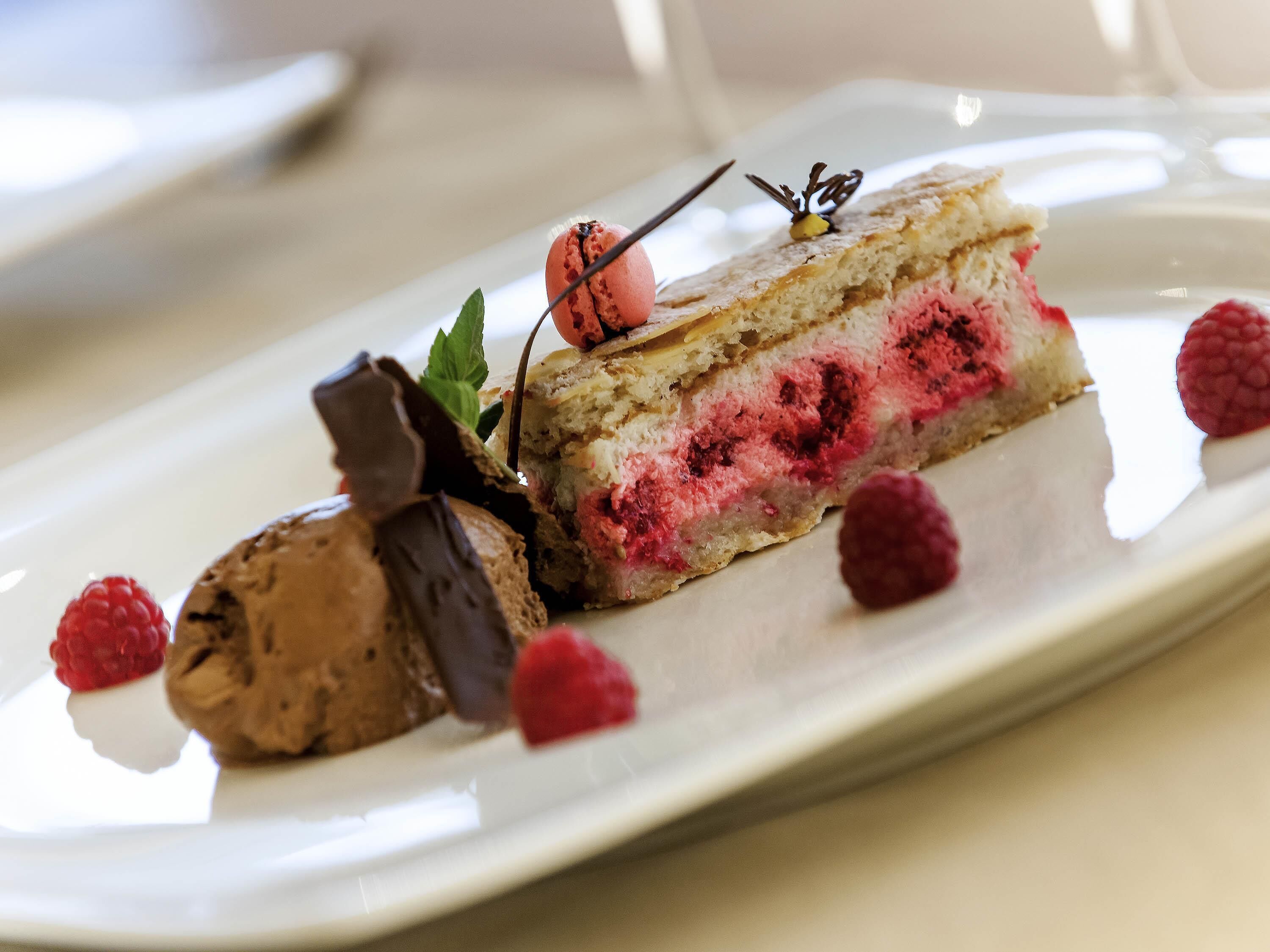A slice of cake with raspberry filling and chocolate decoration on a white plate.