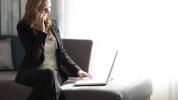A person sitting on a grey sofa with a laptop, in a room with patterned curtains and a modern design.