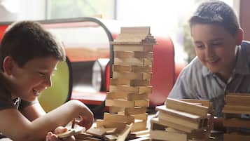 Two children playing with wooden blocks, a red chair, and a window in the background.
