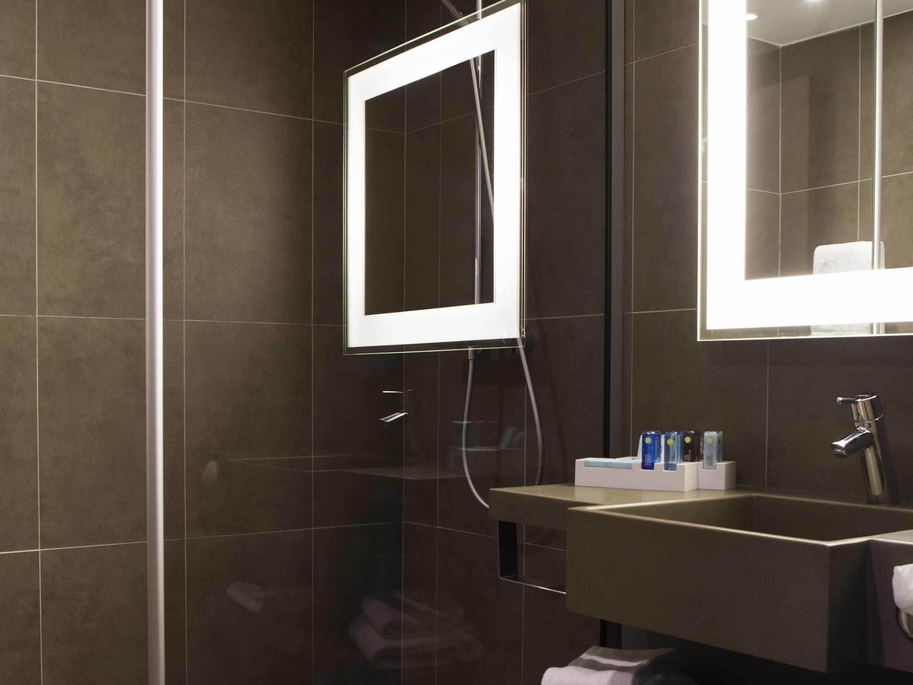 A modern bathroom with dark tiles, a glass shower enclosure, a vanity with a mirror, and a towel rack.