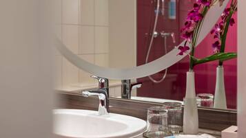 Une salle de bain avec un lavabo blanc, un miroir et un vase contenant des fleurs violettes.