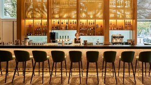 A bar area with a bartender, multiple shelves of liquor bottles, and bar stools. - Dorint Kongresshotel Mannheim (Mannheim)