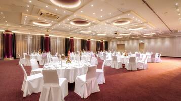 Un salón de banquetes con mesas redondas, manteles blancos y sillas, que incluye una alfombra roja y un diseño moderno del techo.