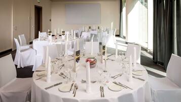 Un salón de conferencias con mesas redondas dispuestas para un evento formal, con manteles blancos, cristalería y cubertería.