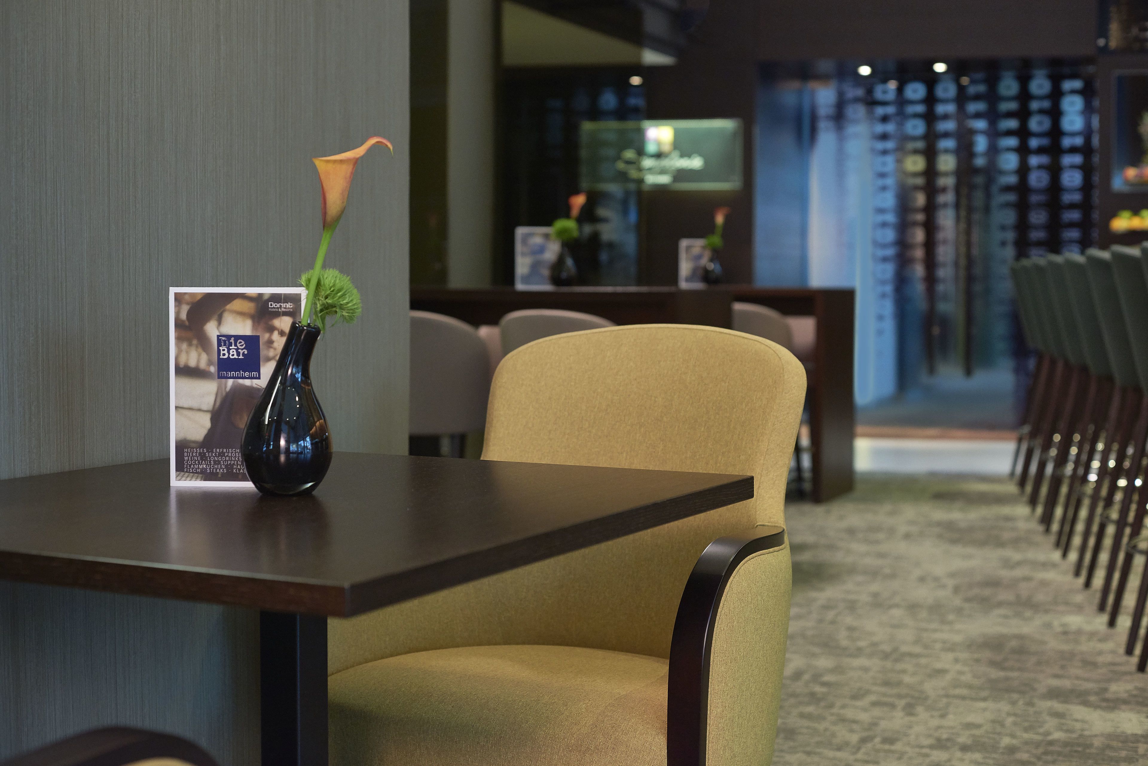 A modern hotel lobby with a reception desk, seating area, and a decorative vase with a flower on a table.