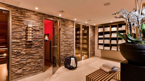 A modern hotel lobby with a stone wall design, a glass door leading to a room, and a large potted orchid plant. - Dorint Kongresshotel Mannheim (Mannheim)