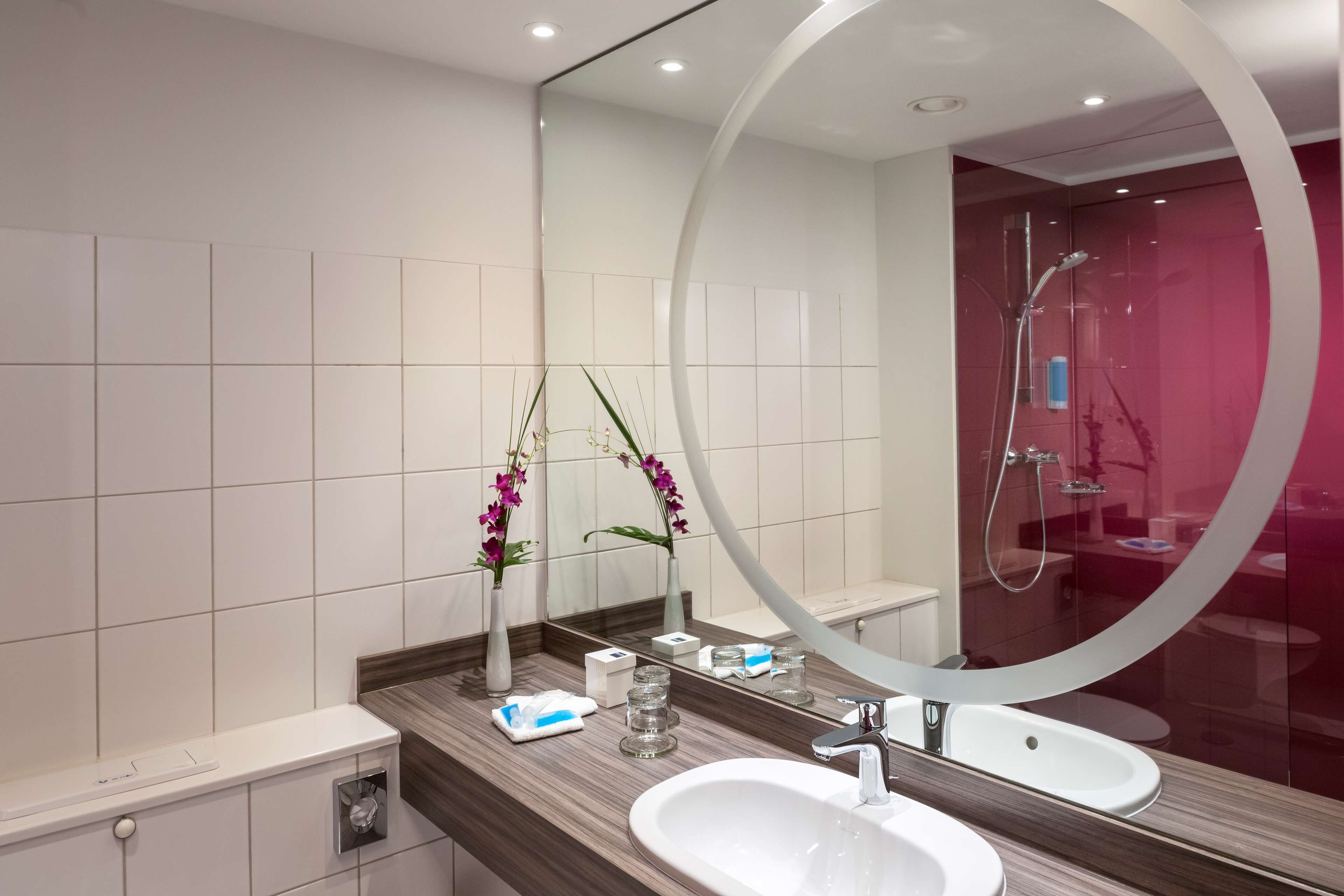 Un baño moderno con un espejo grande, lavamanos blanco y zona de ducha.
