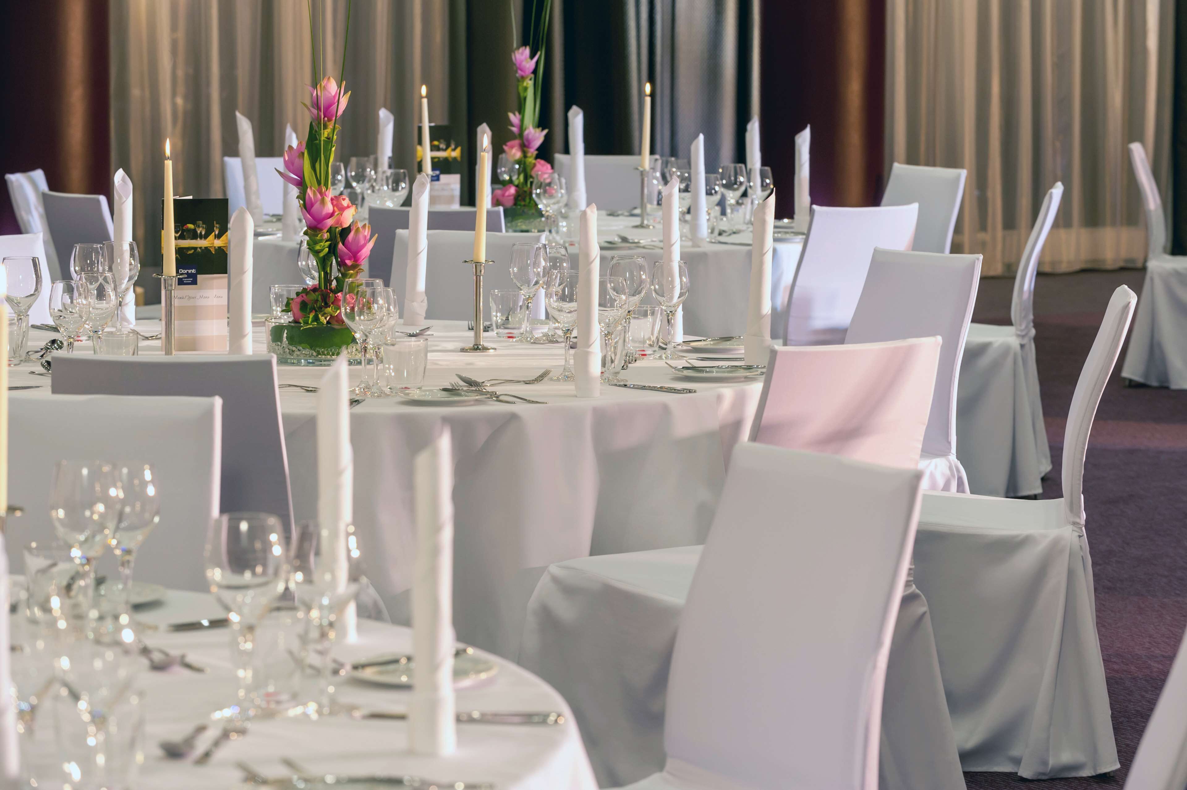 Un salón de banquetes con mesas redondas dispuestas para un evento formal, cada una con mantel blanco, vela y un centro de mesa floral.