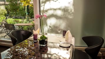 Una mesa de comedor con sillas, un jarrón con flores y un vaso de agua.