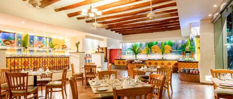 A restaurant with wooden beams, tiled walls, and a large window with a view of greenery. Tables are set with white tablecloths and chairs.