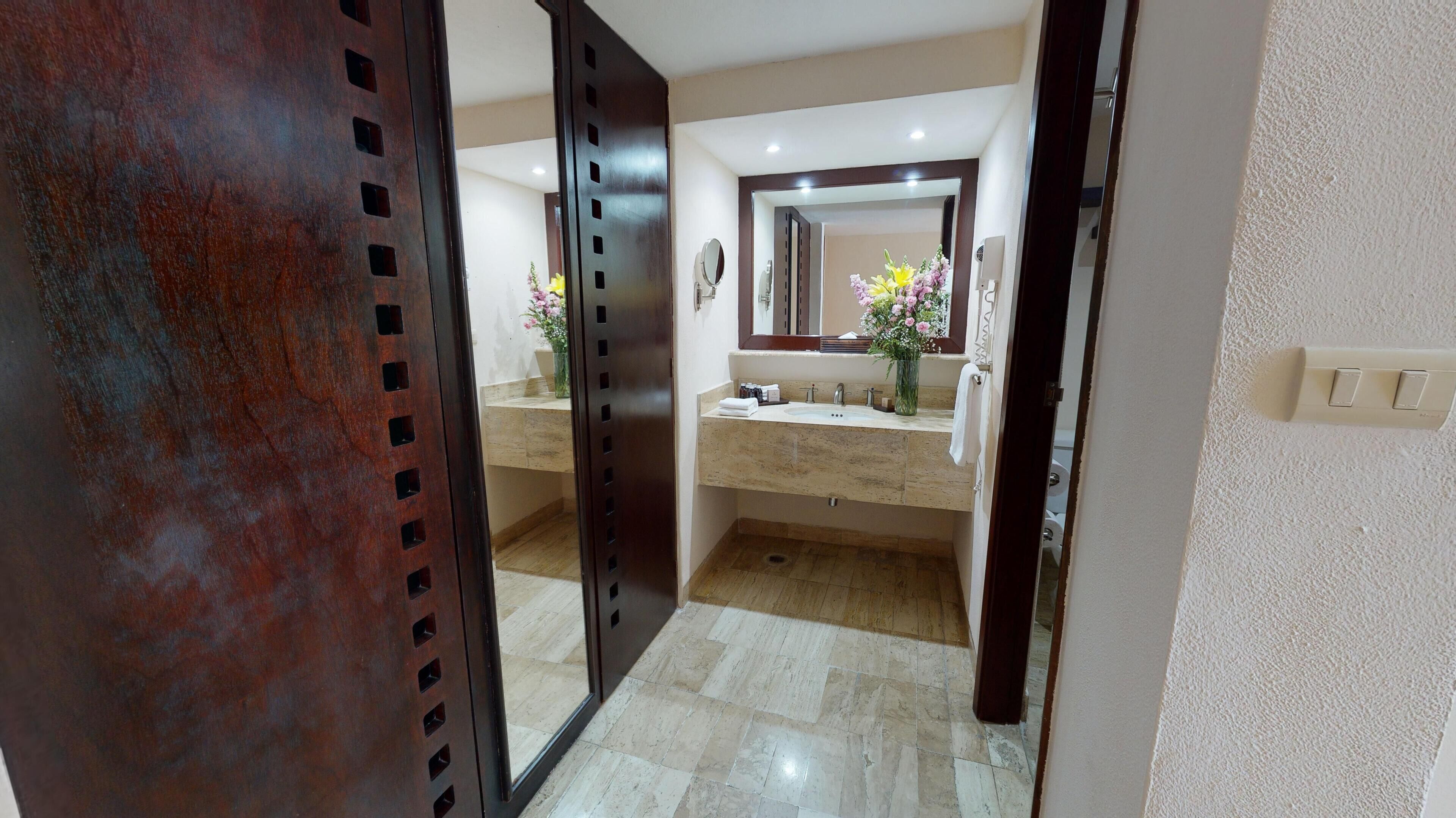Un baño con lavamanos de mármol, espejo y puerta de madera.