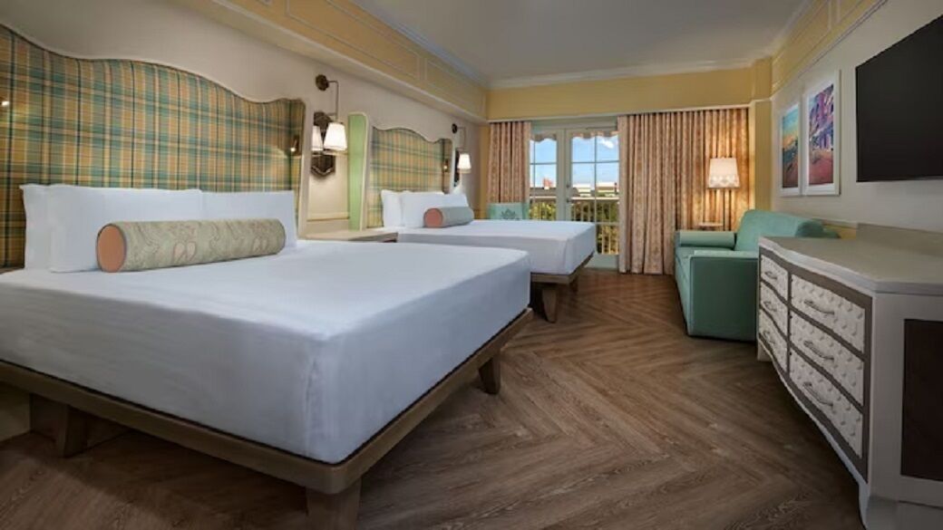 A hotel room with two beds, a sofa, a dresser, and a balcony with curtains.