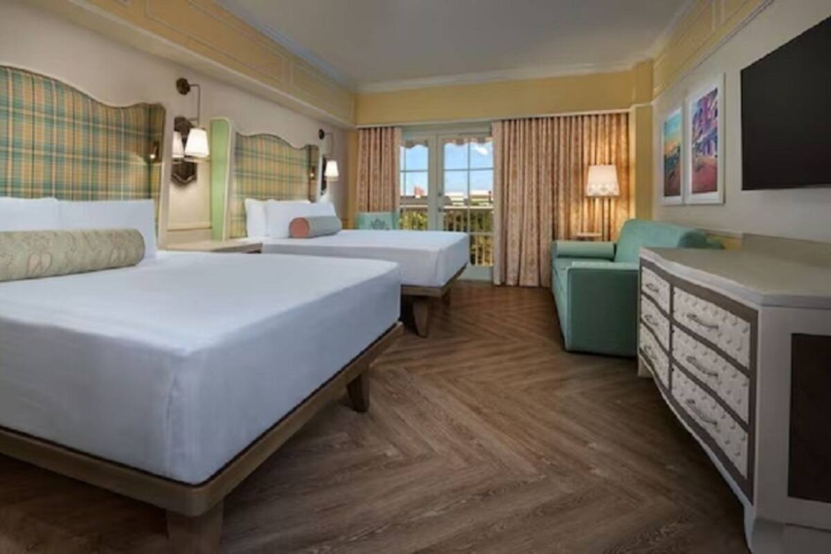 A hotel room with two beds, a sofa, a dresser, and a balcony with curtains.