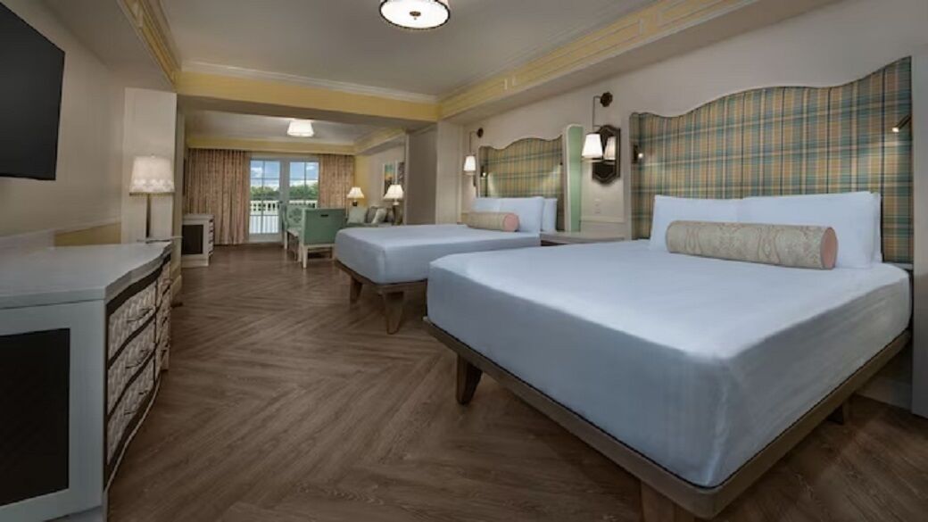 A hotel room with two beds, a desk, a chair, and a balcony with curtains.
