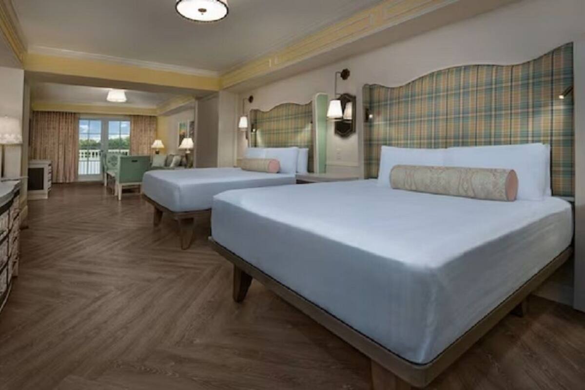 A hotel room with two beds, a desk, a chair, and a balcony with curtains.