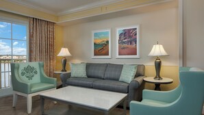 A hotel room with a sofa, two armchairs, a coffee table, and two lamps. There are two framed pictures on the wall.