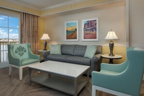 A hotel room with a sofa, two armchairs, a coffee table, and two lamps. There are two framed pictures on the wall.