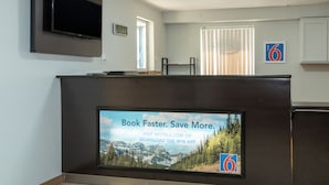 A hotel reception area with a large screen displaying a booking message, a TV mounted on the wall, and a number '6' sign on the wall.