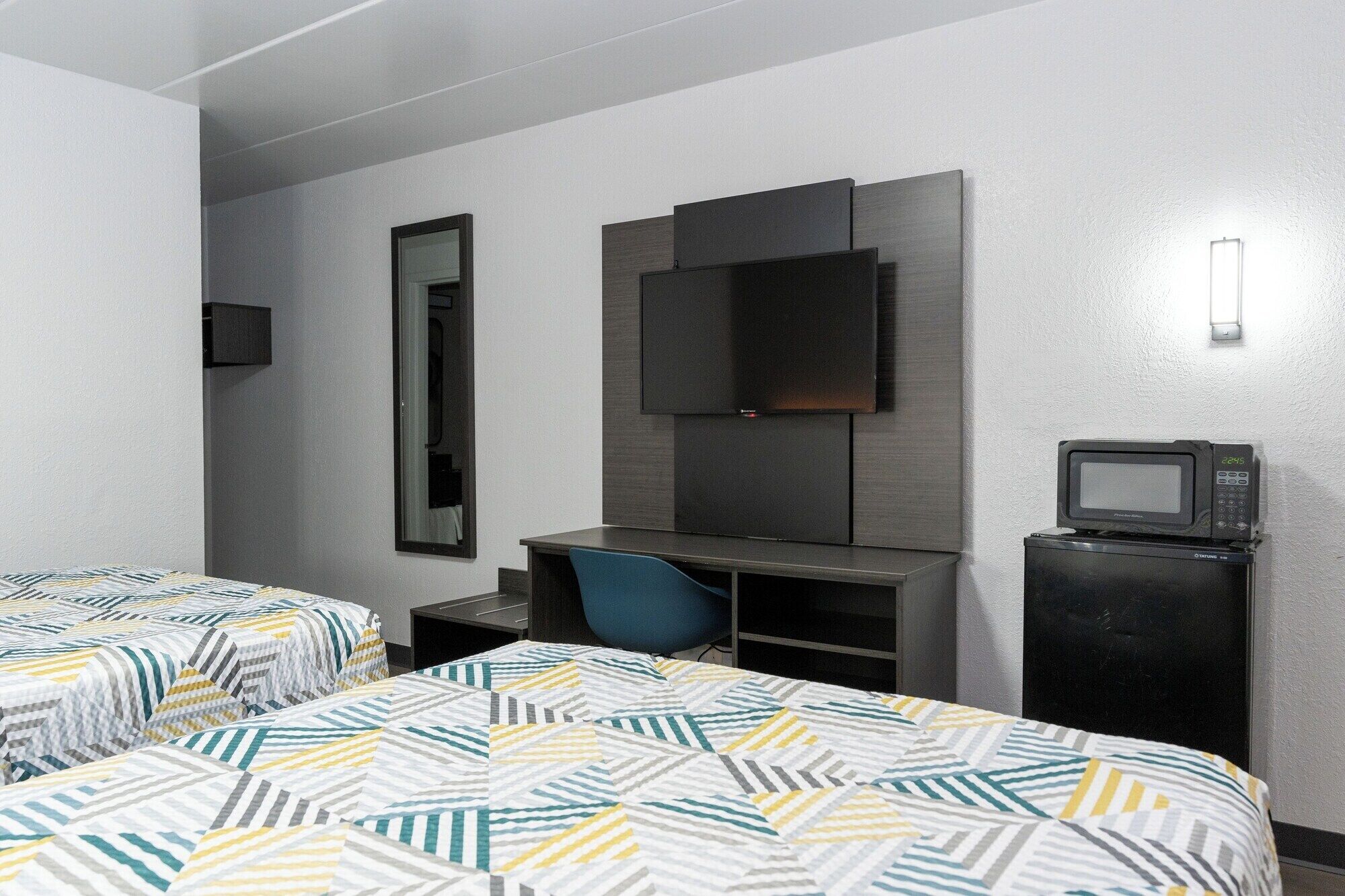 A hotel room with two beds, a desk, a chair, a TV, and a microwave.