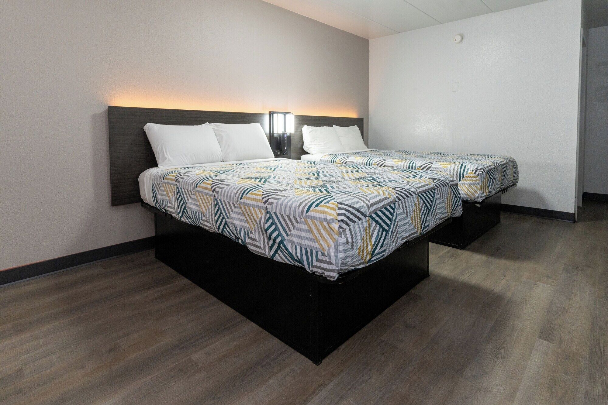 A hotel room with two beds, a dark headboard, and a wall-mounted light.