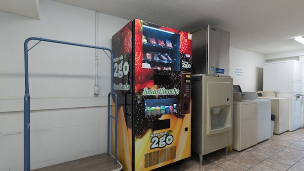 A vending machine labeled 'SmartSnacks' and a small refrigerator in a room with tiled flooring and white walls.
