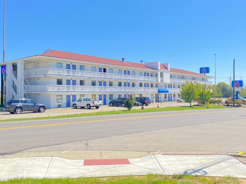Un motel de varios pisos con techo rojo, varias terrazas y un estacionamiento con vehículos.