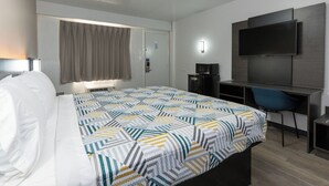 A hotel room with a bed, a desk with a chair, a television, and a window with curtains.