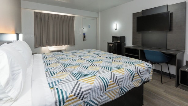 A hotel room with a bed, a desk with a chair, a television, and a window with curtains.