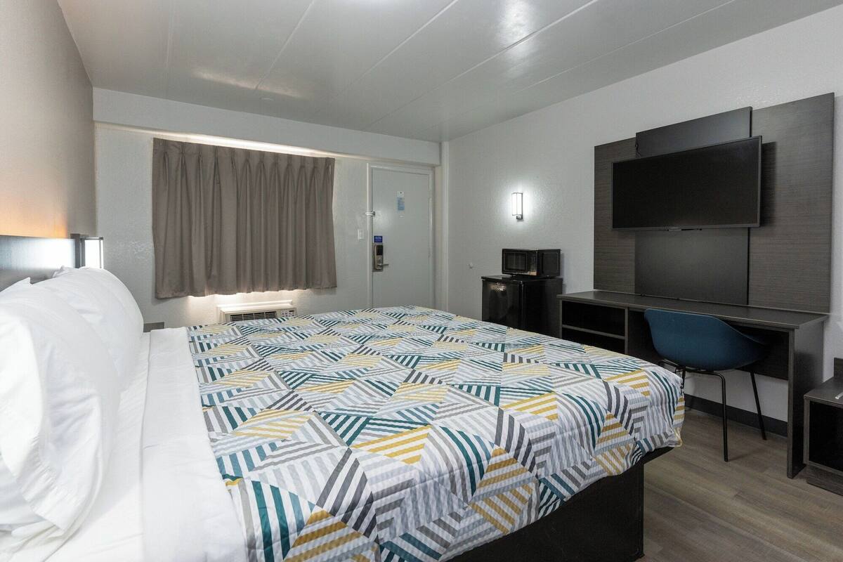Een hotelkamer met een bed, een bureau met stoel, een televisie en een raam met gordijnen.
