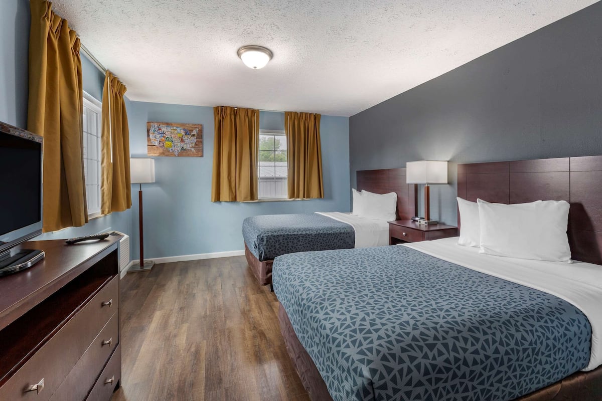 A hotel room with two beds, a TV, a desk, and a window with curtains.