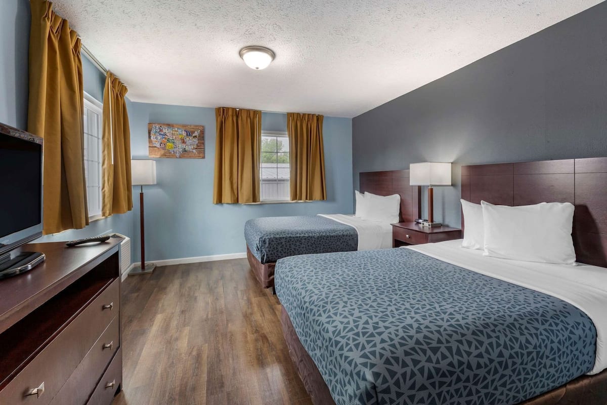 A hotel room with two beds, a desk with a TV, a lamp, and a wall clock.