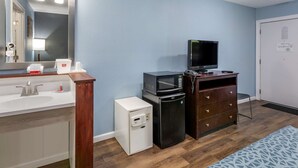 A compact hotel room with a white sink, a small refrigerator, a microwave, a television, and a wooden dresser. - Econo Lodge Inn & Suites Sandusky South (Sandusky)